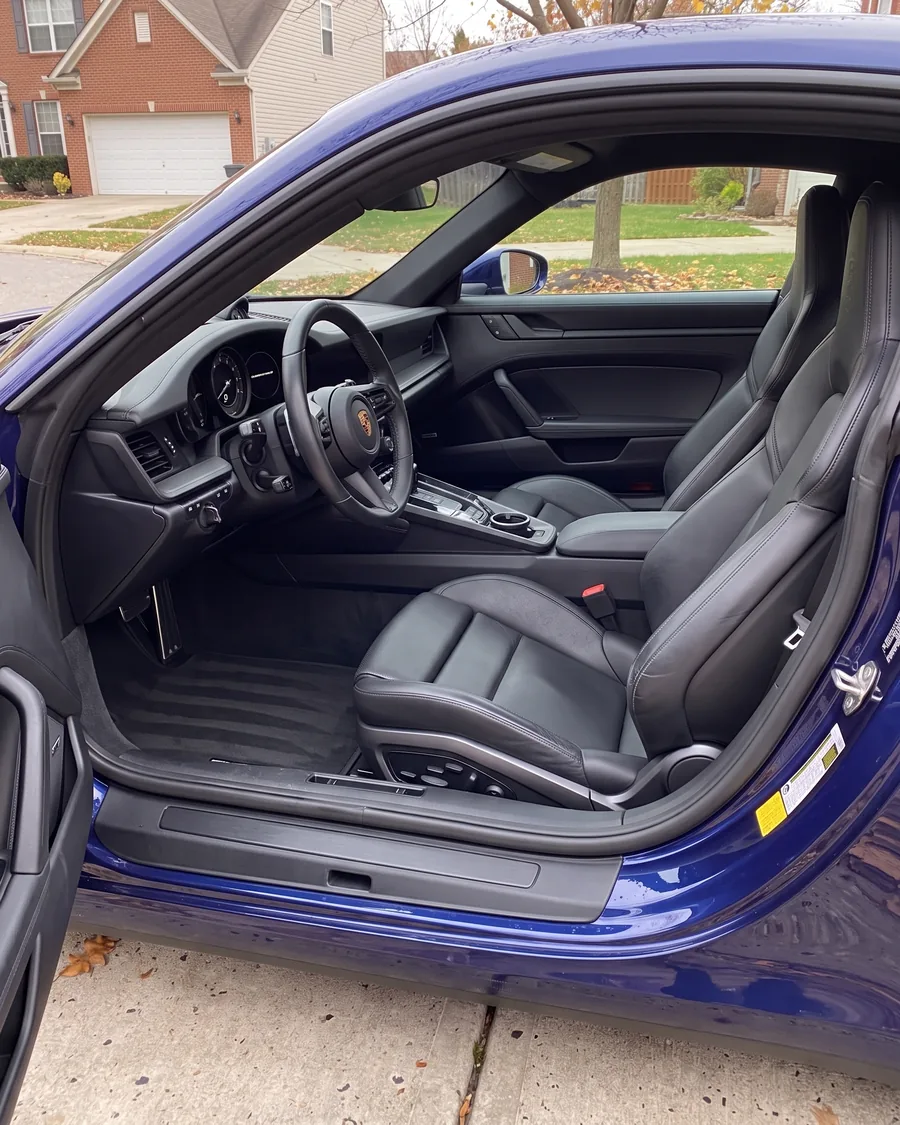 The clean interior of a dark blue sports car through the open driver's door, black leather seats wiped satin