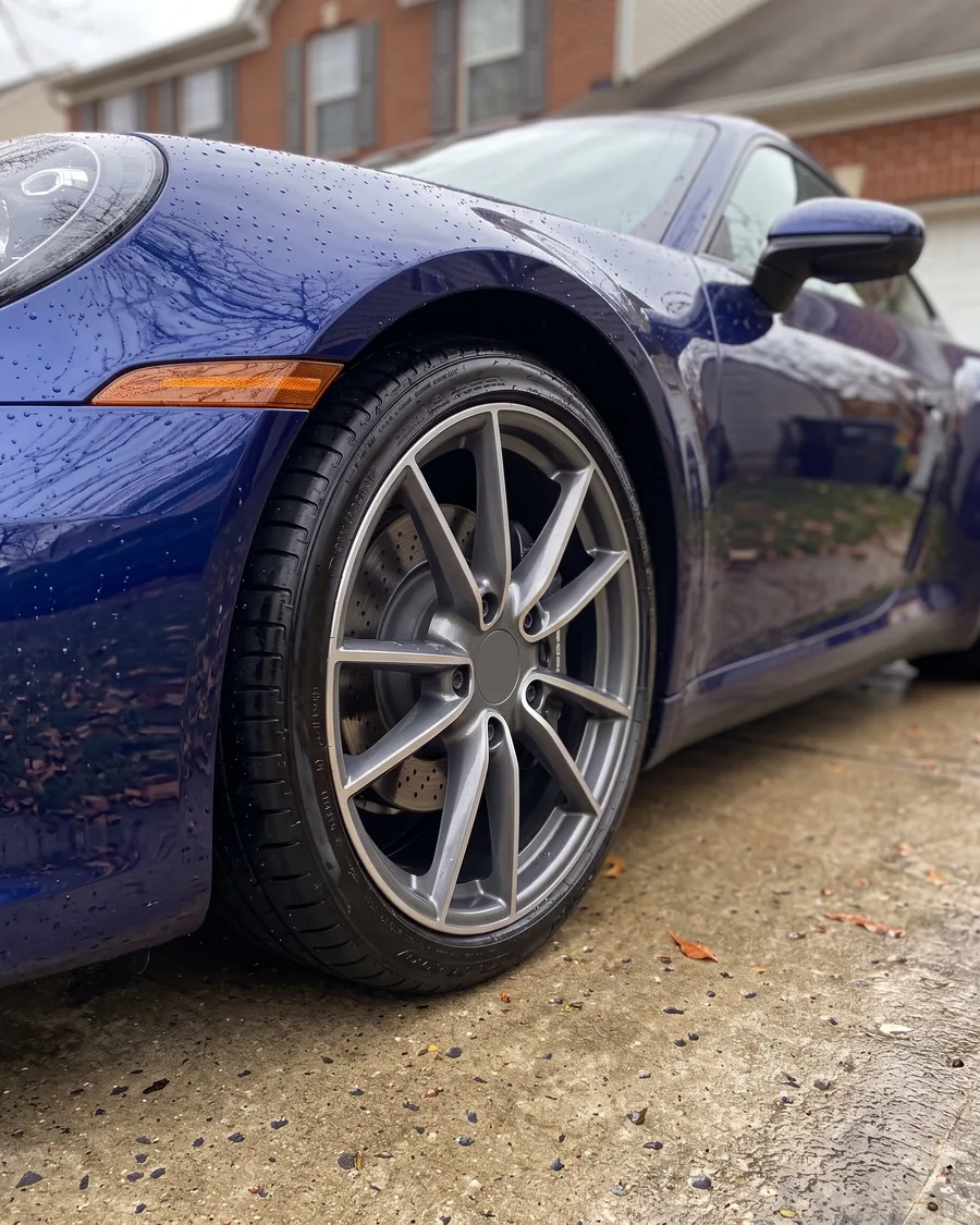 A clean grey alloy wheel and satin tire on a dark blue sports car, water drops on the fender